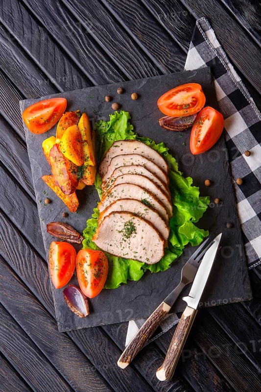 Sliced baked ham with fresh tomatoes on a stone plate in a rustic style