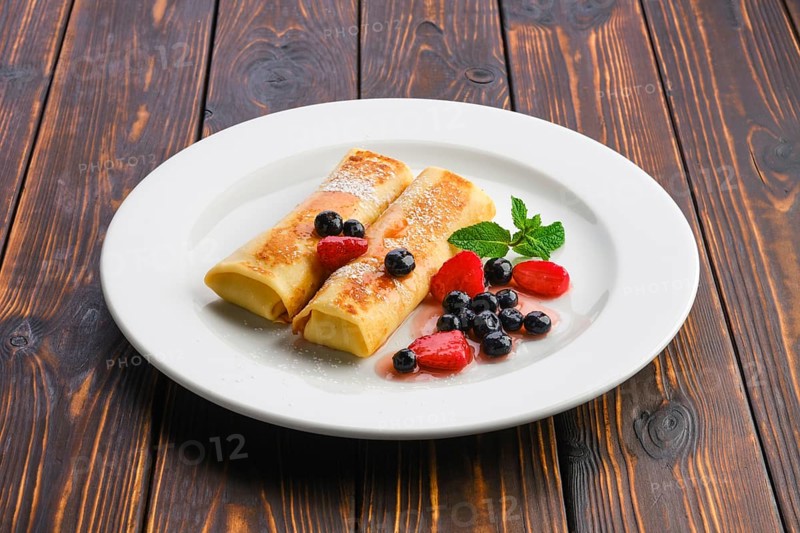 Plate with thin pancakes stuffed with curd and served with berry jam