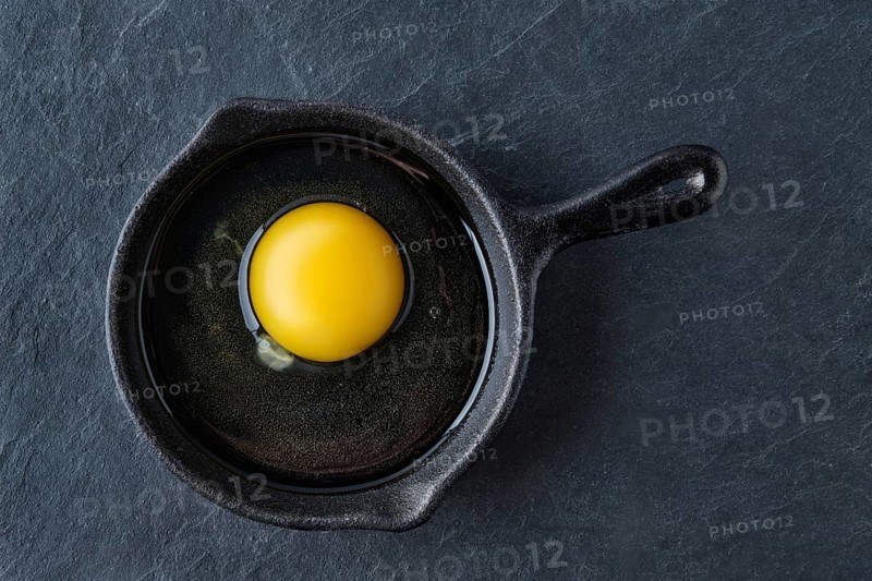 Top view of raw uncooked egg in small cast-iron skillet