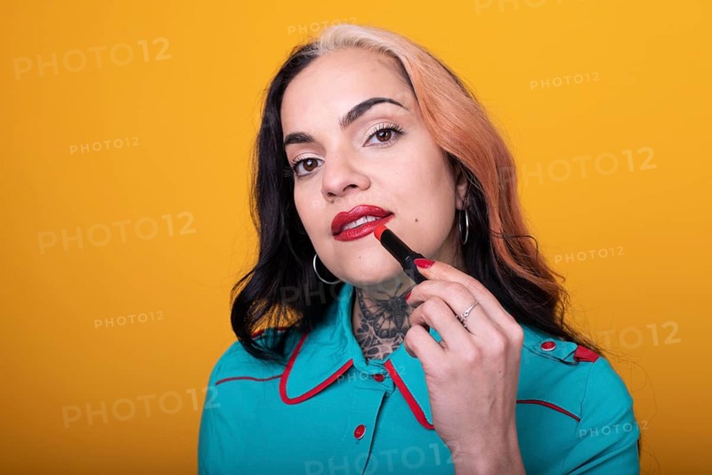 Beautiful caucasian woman applying a bright red color lipstick on her lips over yellow background