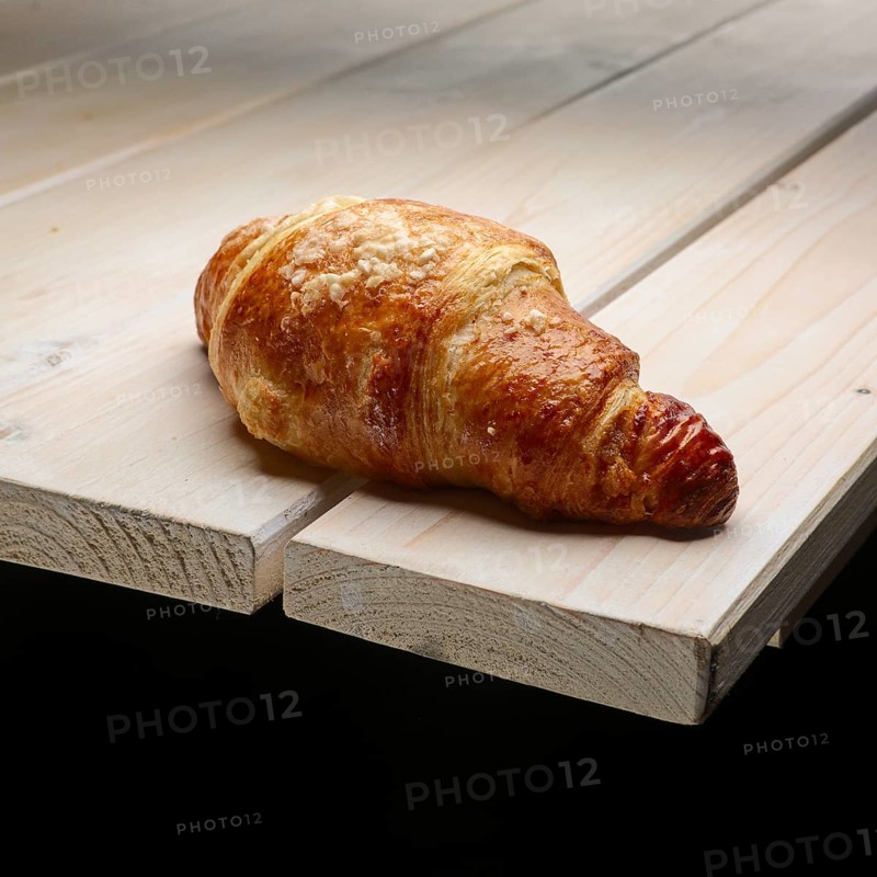 Fresh crisp croissant with powdered sugar on the corner of wooden table