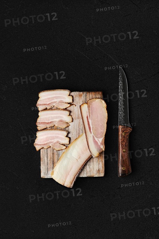 Assortment of slices of smoked pork bacon and lard on wooden cutting board