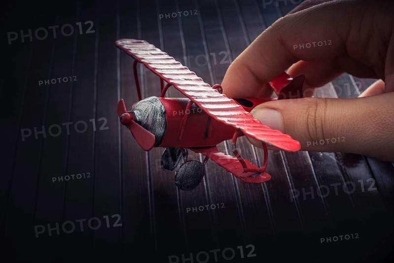 Hand holding a red toy plane on a on wooden texture