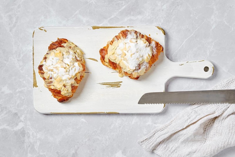 Top view of crispy croissant with caramel and peanut shavings on white serving board on marble background