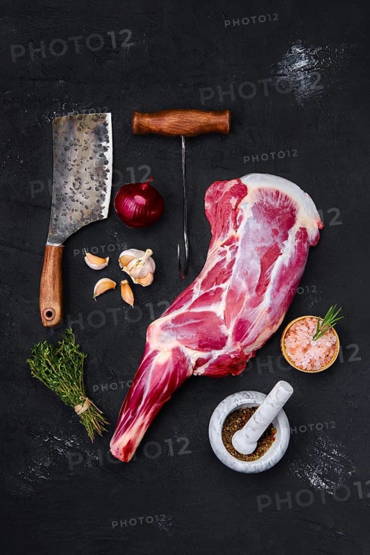 Fresh raw lamb leg bone in on wooden cutting board with herbs and seasoning