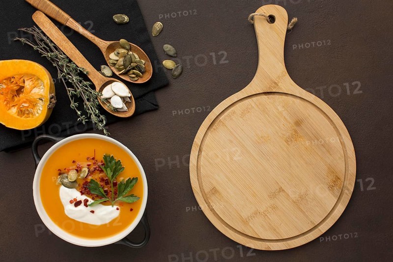 Flat lay of winter squash soup in bowl with chopping board and spoons