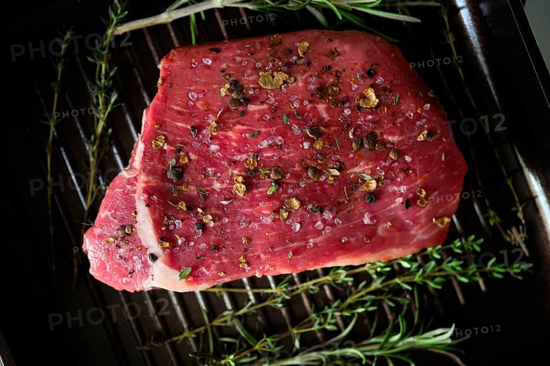Top view of raw steak with spices on grilling pan