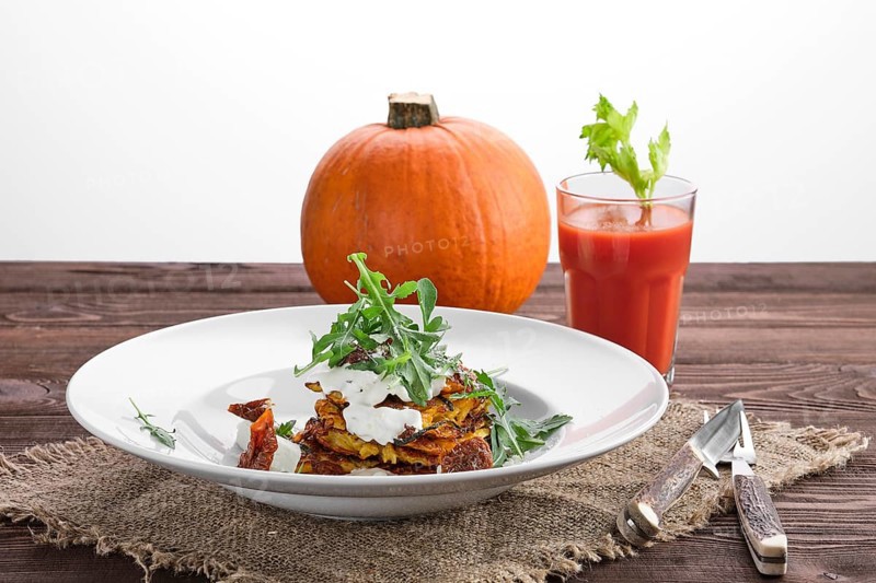 Pumpkin fritters with sour cream with whole pumpkin and tomato juice on background