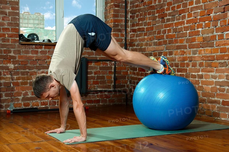 Athletic man doing balancing exercises with the gym ball. Fitness workout