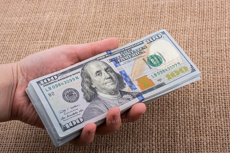 Hand holding banknote bundle of US dollar on a linen canvas background