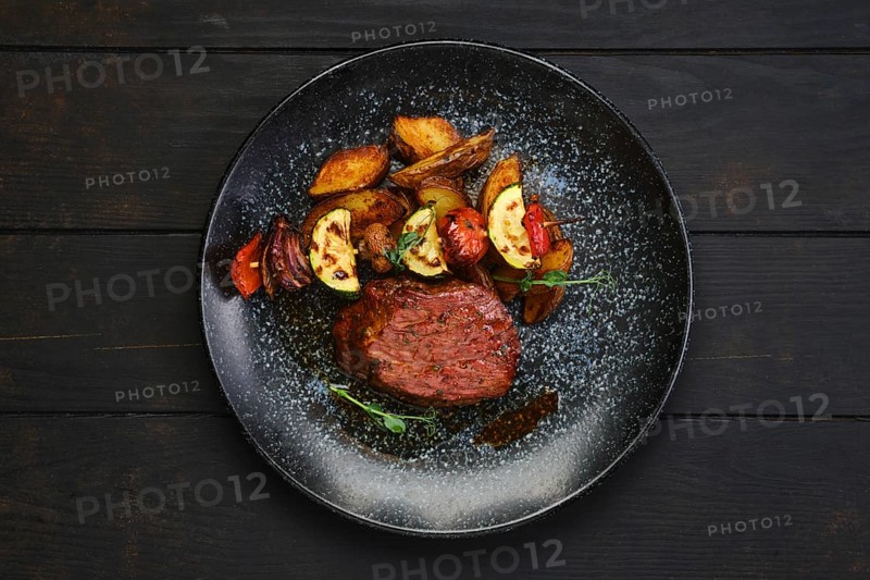 Top view of juicy beef steak with potato wedges and grilled vegetables on skewer