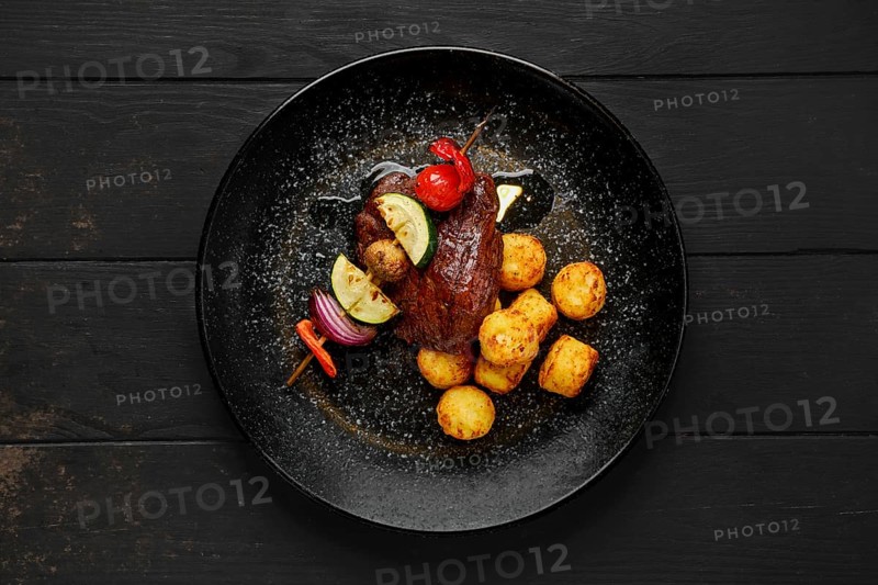 Top view of grilled beef with vegetables and potato balls on a plate