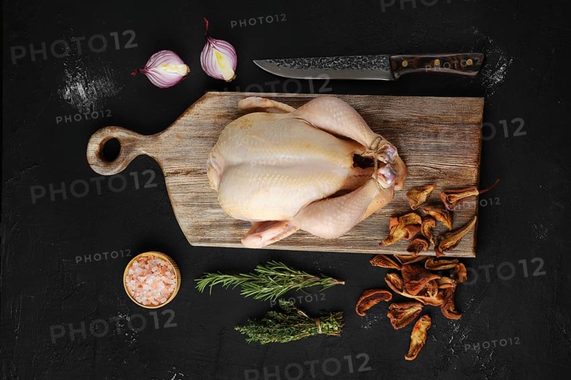 Raw whole broiler chicken with spices on wooden cutting board
