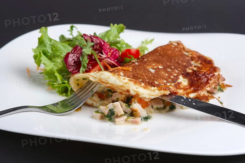 Cutting with knife omelet with ham and vegetables