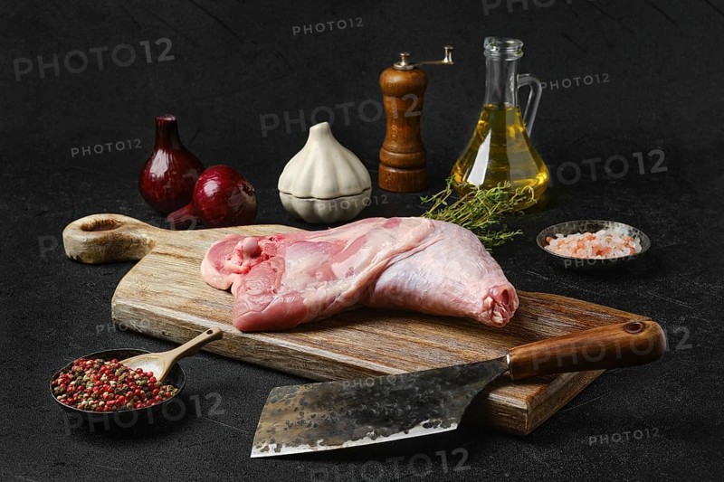 Raw turkey leg with skin on cutting board with cooking ingredients on black background