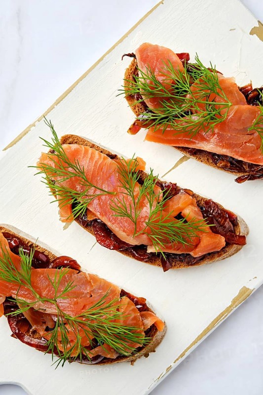 Top view of salmon sandwich with caramelized onion on wooden serving board