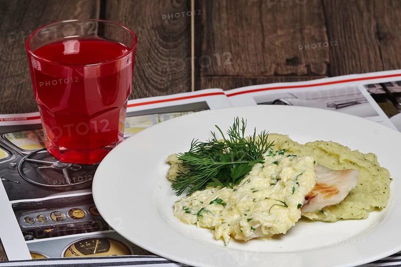 Fried fish and mashed potato with glass of fruit-drink on wooden table