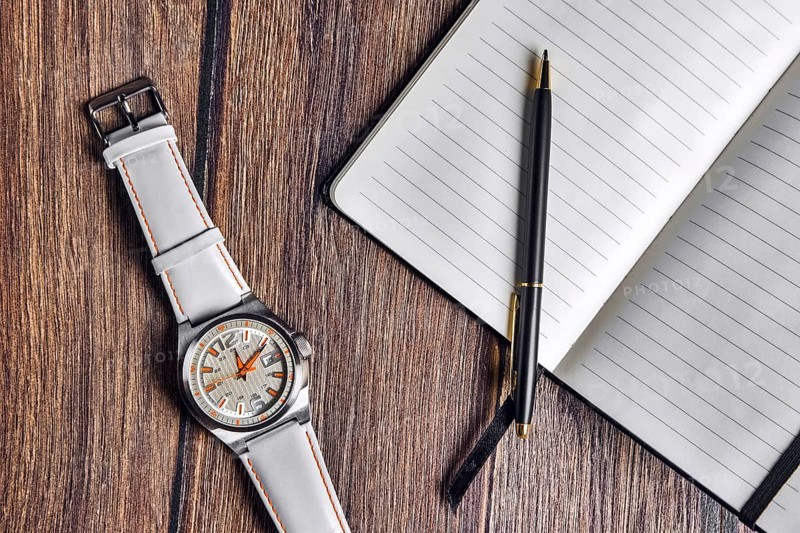 Top view of open blank notebook with pen and wrist watch on wooden table