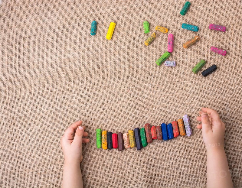 Toddlers hand putting crayons in line on canvas