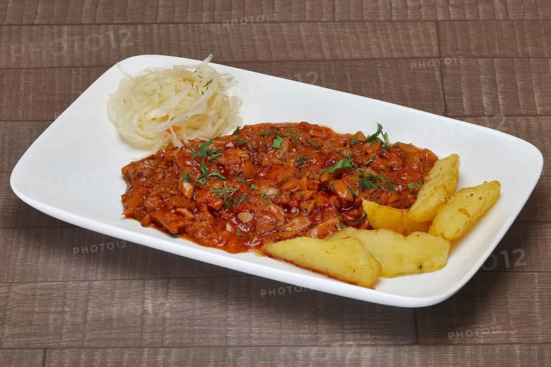 Beef goulash with potato wedges and pickled cabbage on wooden table
