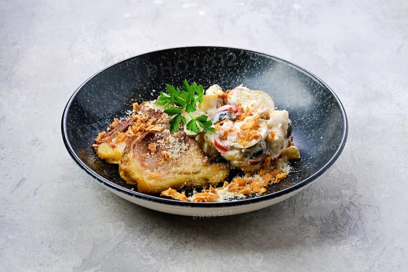 Pickled cucumber with boiled potato and olives served with fried pork belly slices on a plate