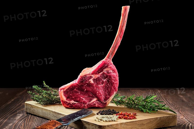Raw juicy cowboy steak on wooden cutting board with spice
