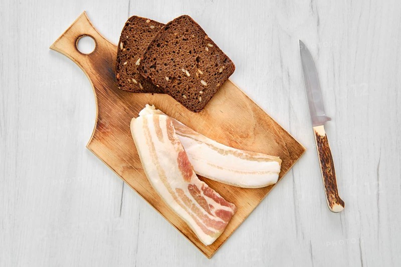 Top view of two slices of bacon and brown bread on wooden cutting board