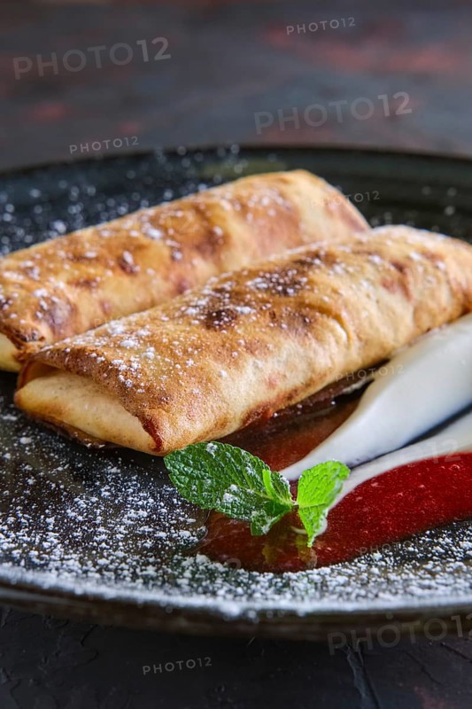 Sweet pancakes stuffed with curd and decorated with sour cream and strawberry jam