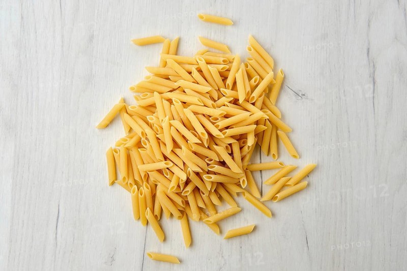 Overhead view of penne pasta on wooden background