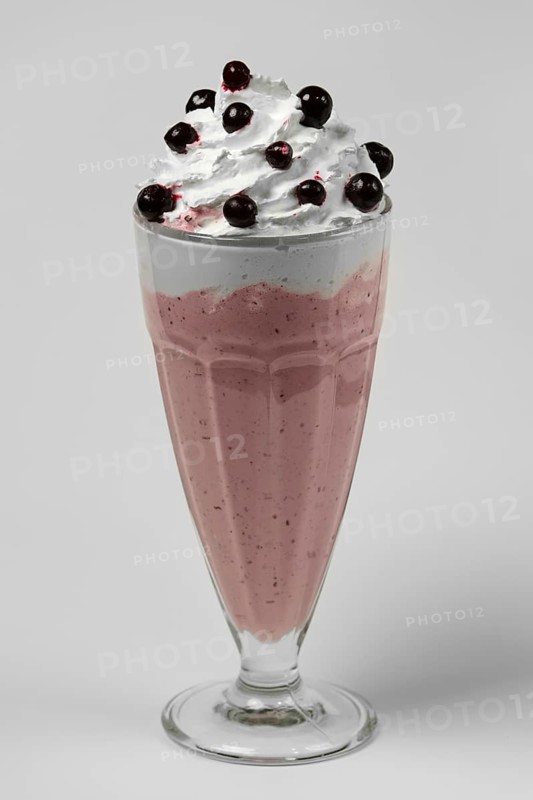 Milkshake black currant summer cocktail in tall facetted glass on gray background