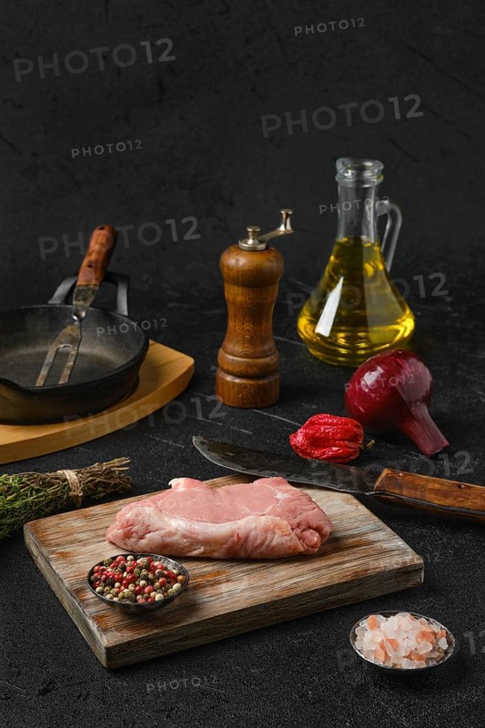 Raw veal steak bone in with ingredients for cooking on black background