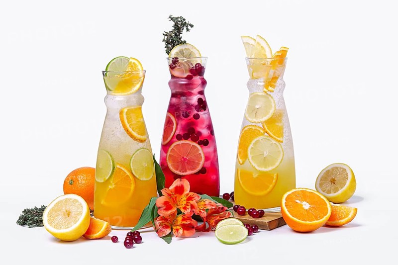 Three pitchers with summer fruit and berry cocktails on white background