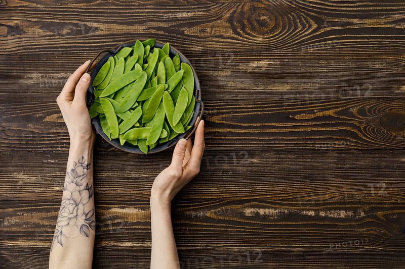 Overhead view of fresh green peas in a pods in hand over wooden background