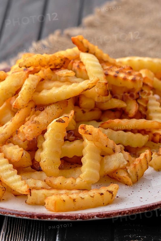 Fried crinkle cut french fries on dark wooden table