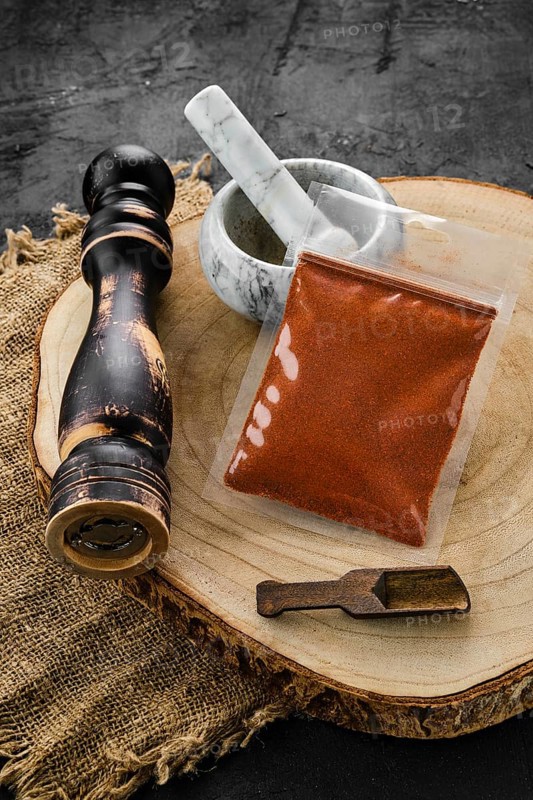 Wooden cross section with chilli pepper in plastic package and stone mortar and mill