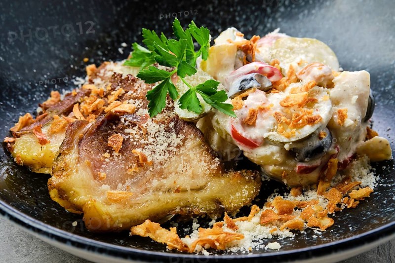 Closeup view of pickled cucumber with boiled potato and olives served with fried pork belly slices on a plate