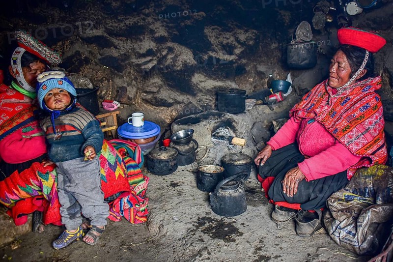 Quechua Indians in traditional dress cooking at the fireplace of their hut