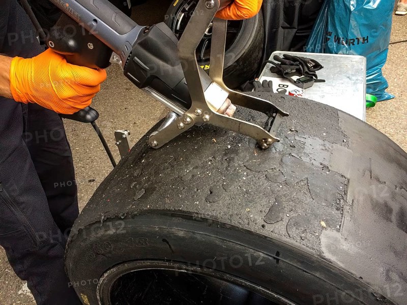 Race mechanic cleans surface of racing tyres slicks makes reconditioning spreads used tyres again for reuse at car races