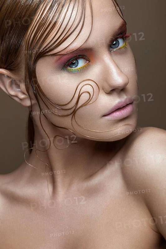 Beautiful girl with bright colored makeup and wet strands of hair on the face. Creative image. Picture taken in the studio