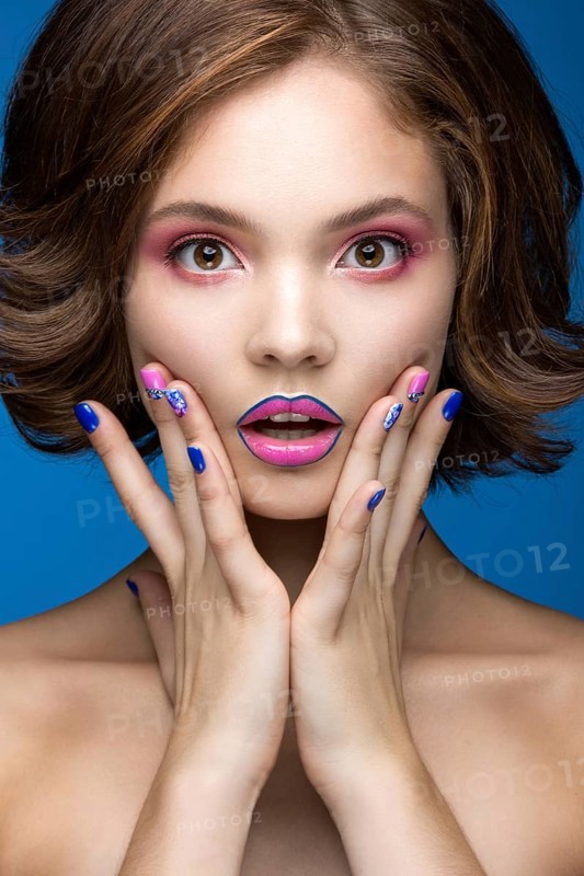 Beautiful model girl with bright makeup and colored nail polish. Beauty face. Short colorful nails. Picture taken in the studio on a blue background