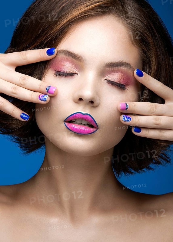 Beautiful model girl with bright makeup and colored nail polish. Beauty face. Short colorful nails. Picture taken in the studio on a blue background