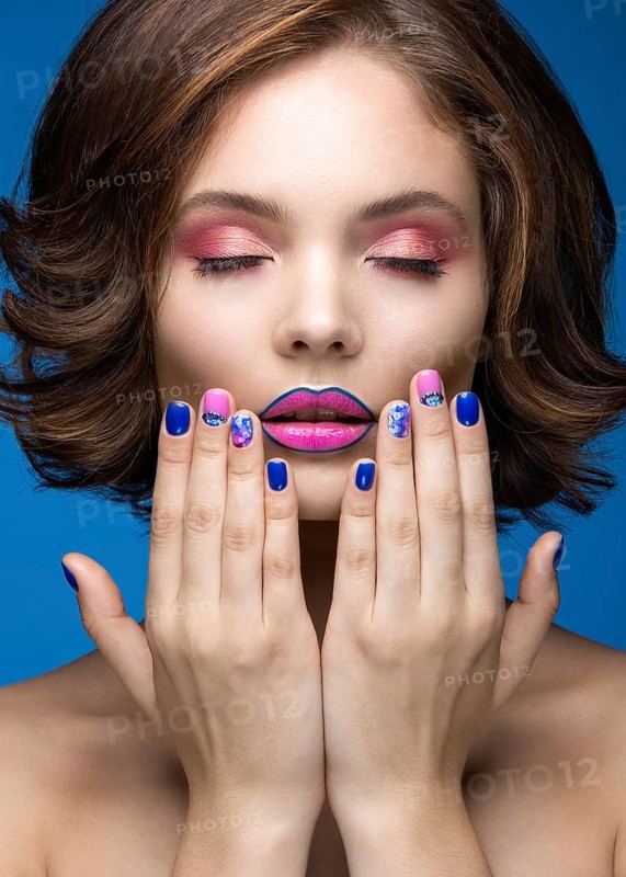 Beautiful model girl with bright makeup and colored nail polish. Beauty face. Short colorful nails. Picture taken in the studio on a blue background