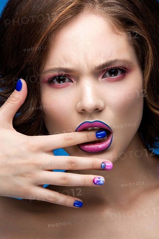 Beautiful model girl with bright makeup and colored nail polish. Beauty face. Short colorful nails. Picture taken in the studio on a blue background