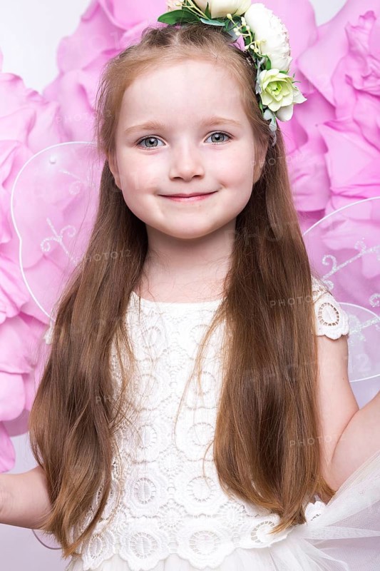 Little fairy girl in white dress on a background of flowers. Photo taken in studio