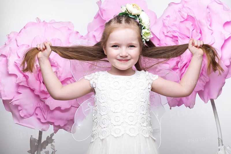 Little fairy girl in white dress on a background of flowers. Photo taken in studio