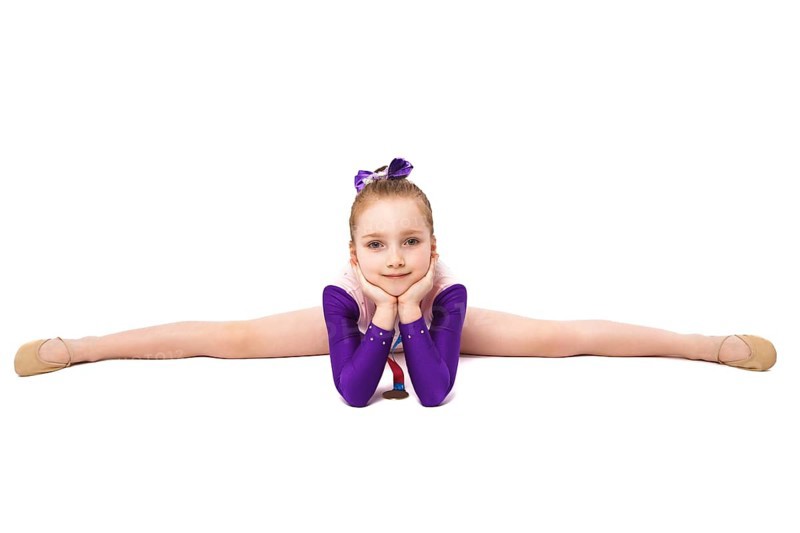 Little girl gymnast with a medal in a sports swimsuit doing exercises. Photo taken in the studio on a white background