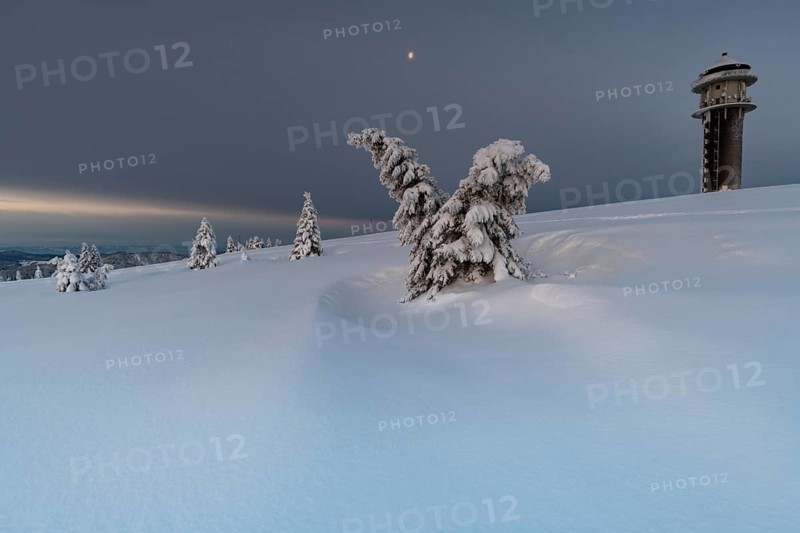 Snow-covered trees and landscape and the new Feldberg tower on the Feldberg in front of sunrise
