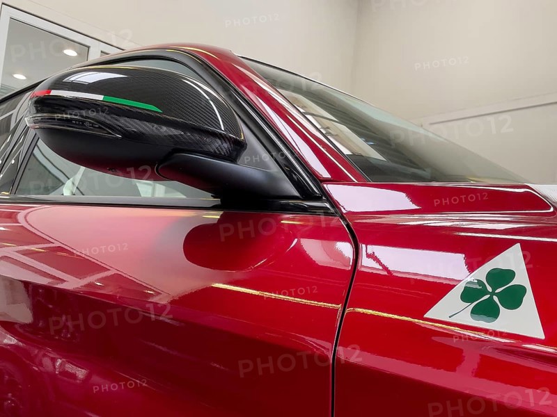 Detail of rear view mirror with carbon optic fairing with coloured stripes of Italian national colour flag Tricolore historical modern signet logo marking of Alfa Romeo Quadrifoglio green four-leaf clover on white triangle for sporty cars race car on limited to 500 pieces Italian sports car Alfa Romeo Giulia GTAm