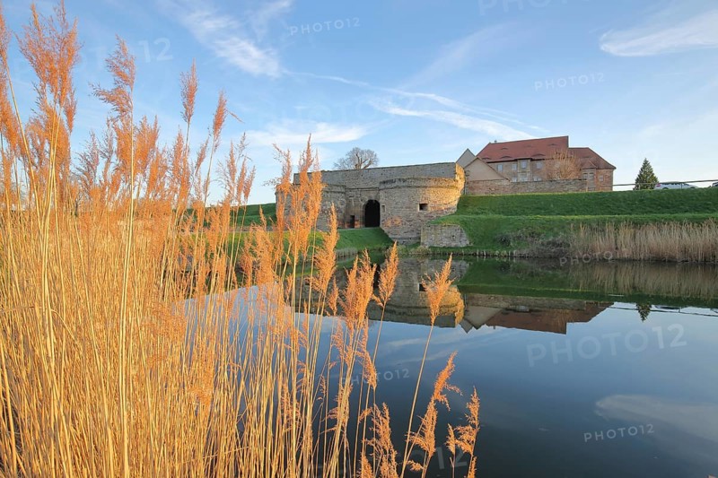 Renaissance moated castle with reflection in the pond and golden reed grass
