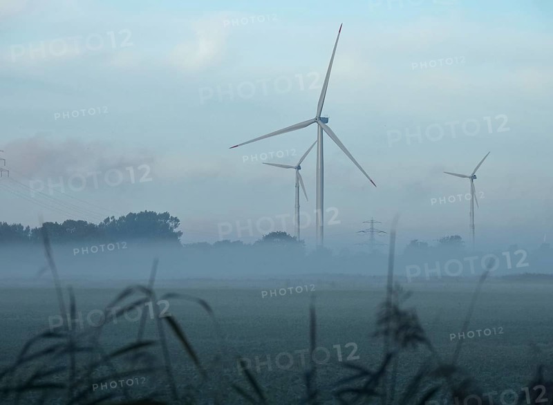 Wind turbines and the mast of a high-voltage power line in the early morning fog. Ochsenwerder